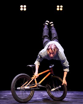 Tanssija tasapainottelee BMX-pyörän päällä käsillään.