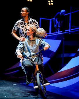 Two performers are riding a bicycle together.