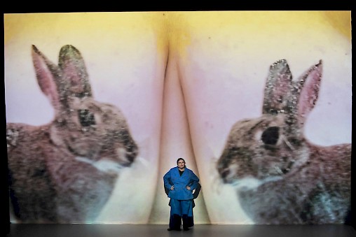 Katy stands on stage and behind her is projected a picture of bunny tattoos.