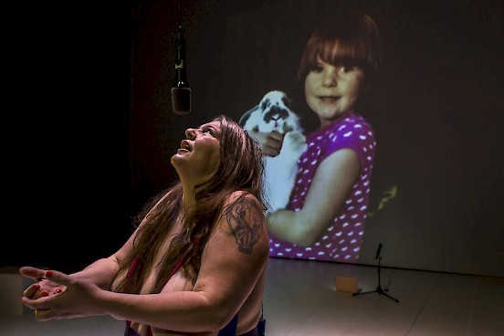 Katy looks at the audience and behind her is projected a picture of her as a child holding a bunny.